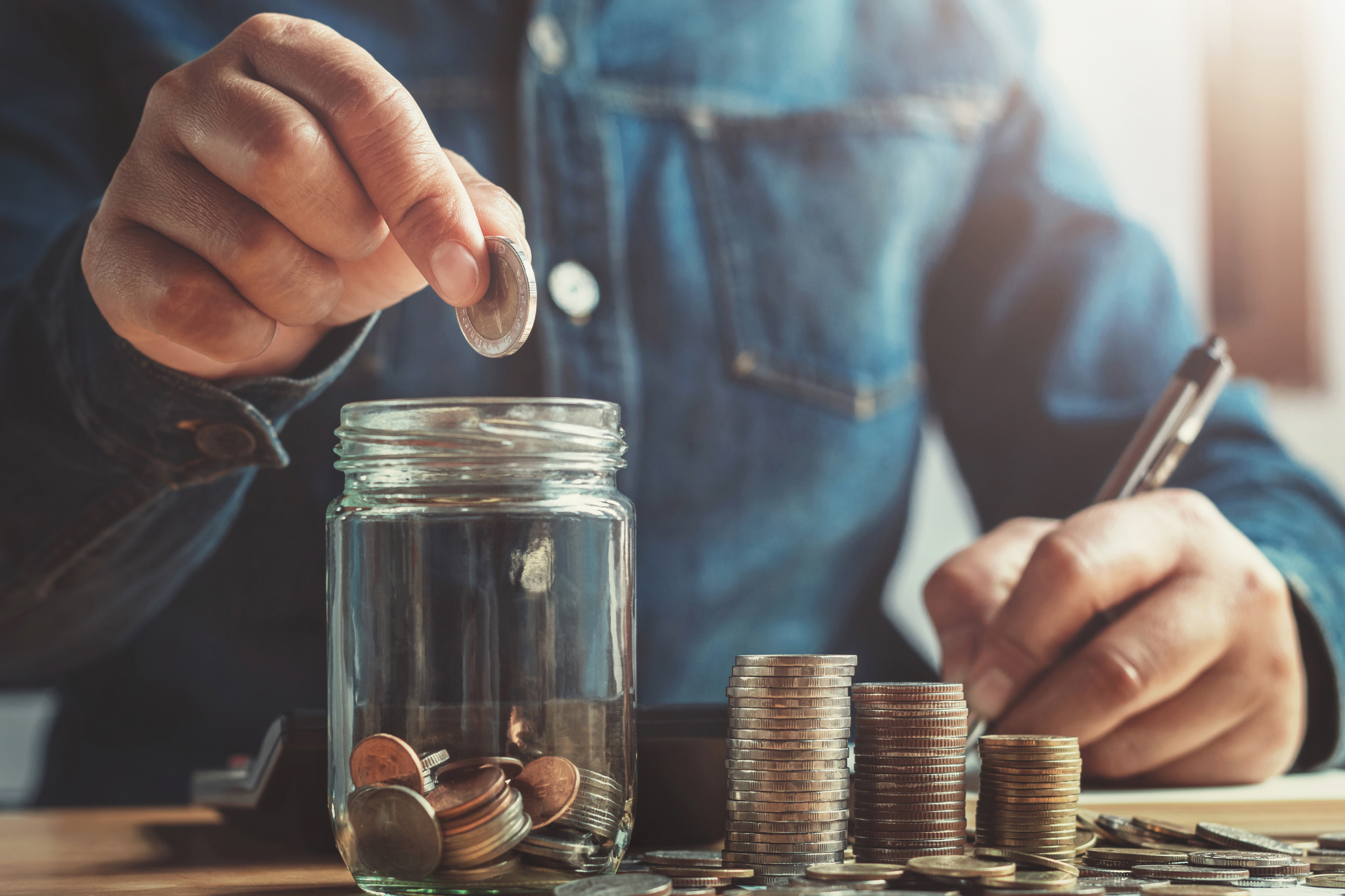 hand puting coins into jug glass for saving money finance and accounting concept
