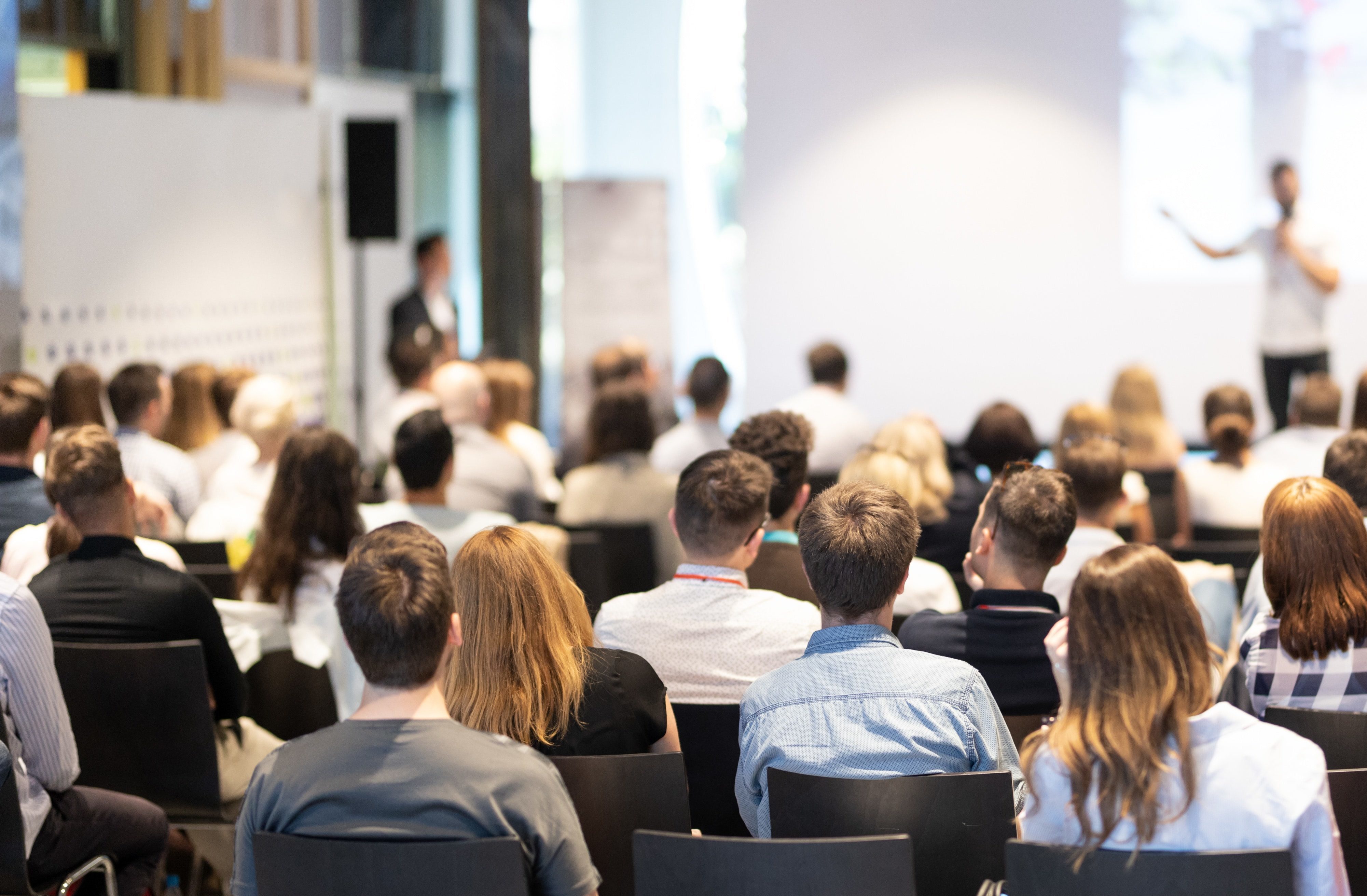 Speaker giving a talk in conference hall at business event. Audience at the conference hall. Business and Entrepreneurship concept. Focus on unrecognizable people in audience.